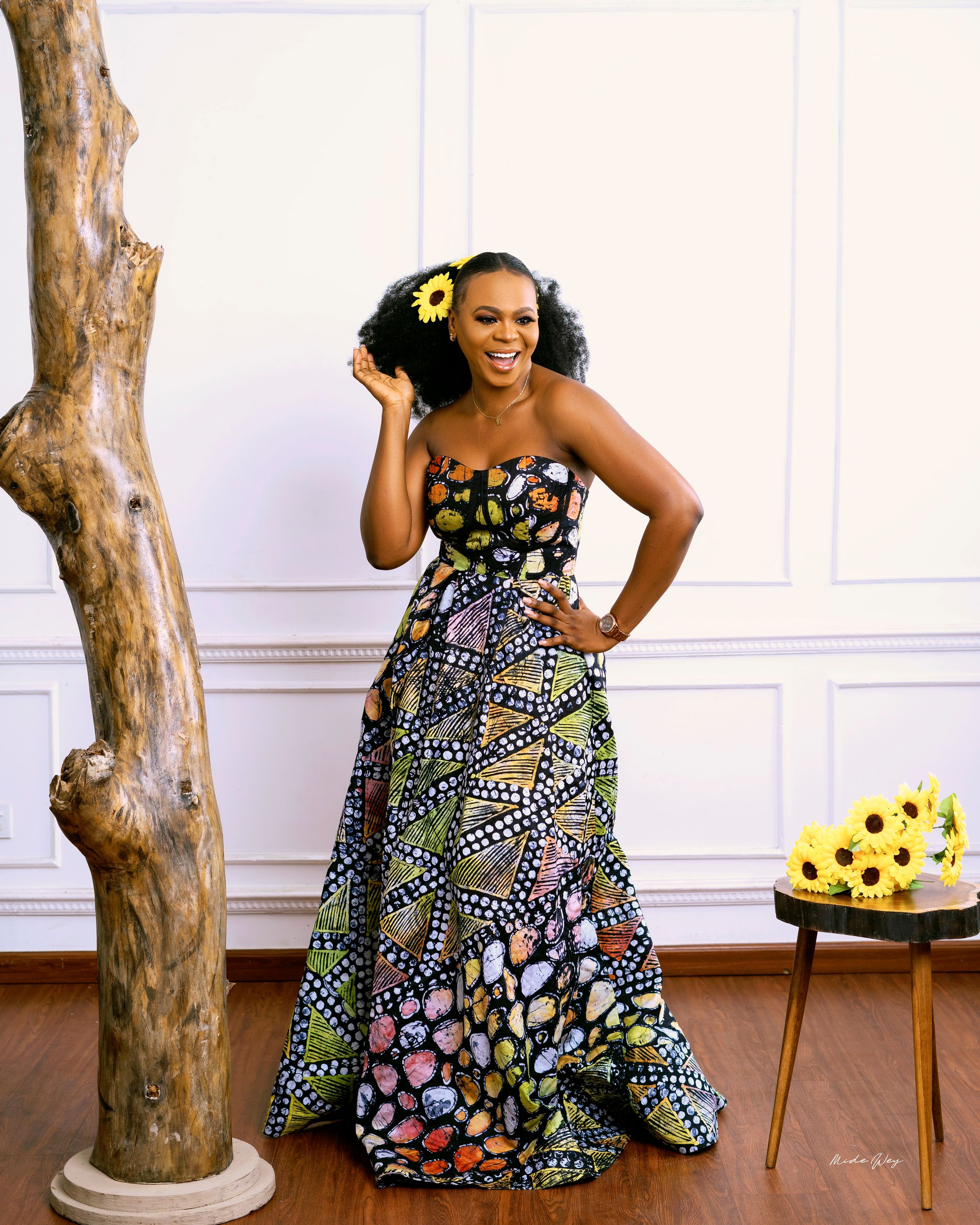 Joyful pose in colorful patterned ball gown next to decorative tree trunk.