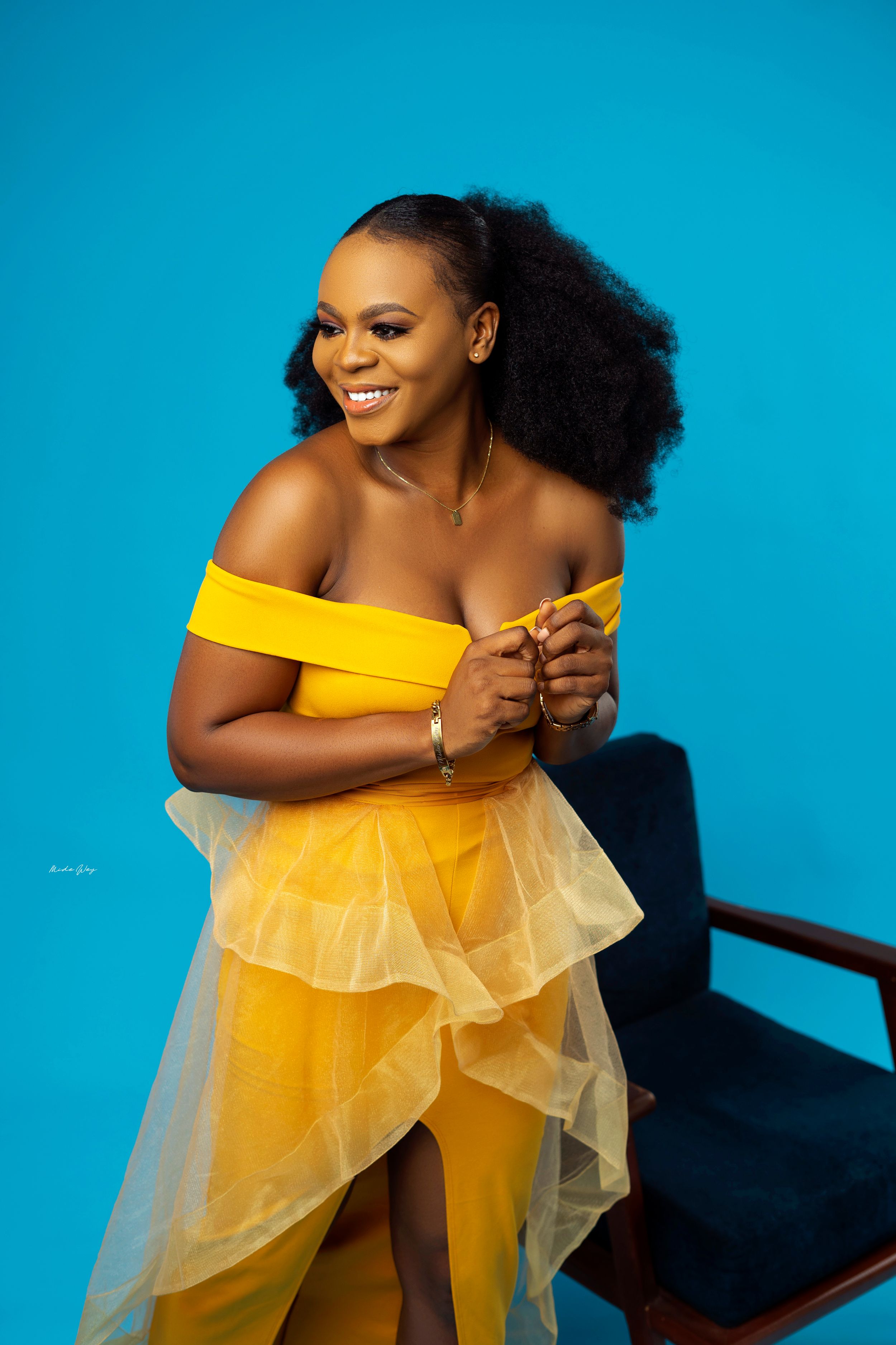 Vibrant portrait in yellow off-shoulder gown against bright blue background.