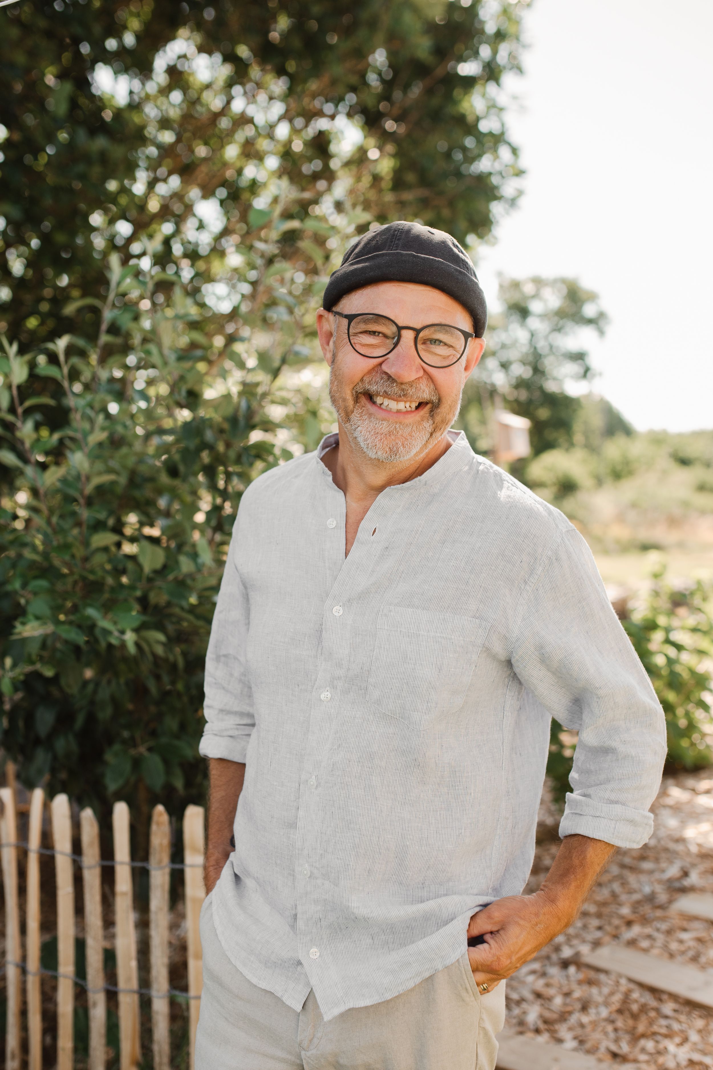 Casual outdoor portrait of a man in linen shirt and cap smiling in natural sunlight.