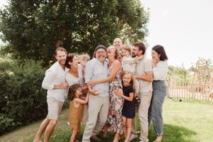 Large family group laughing together during outdoor photo session in summer garden setting.