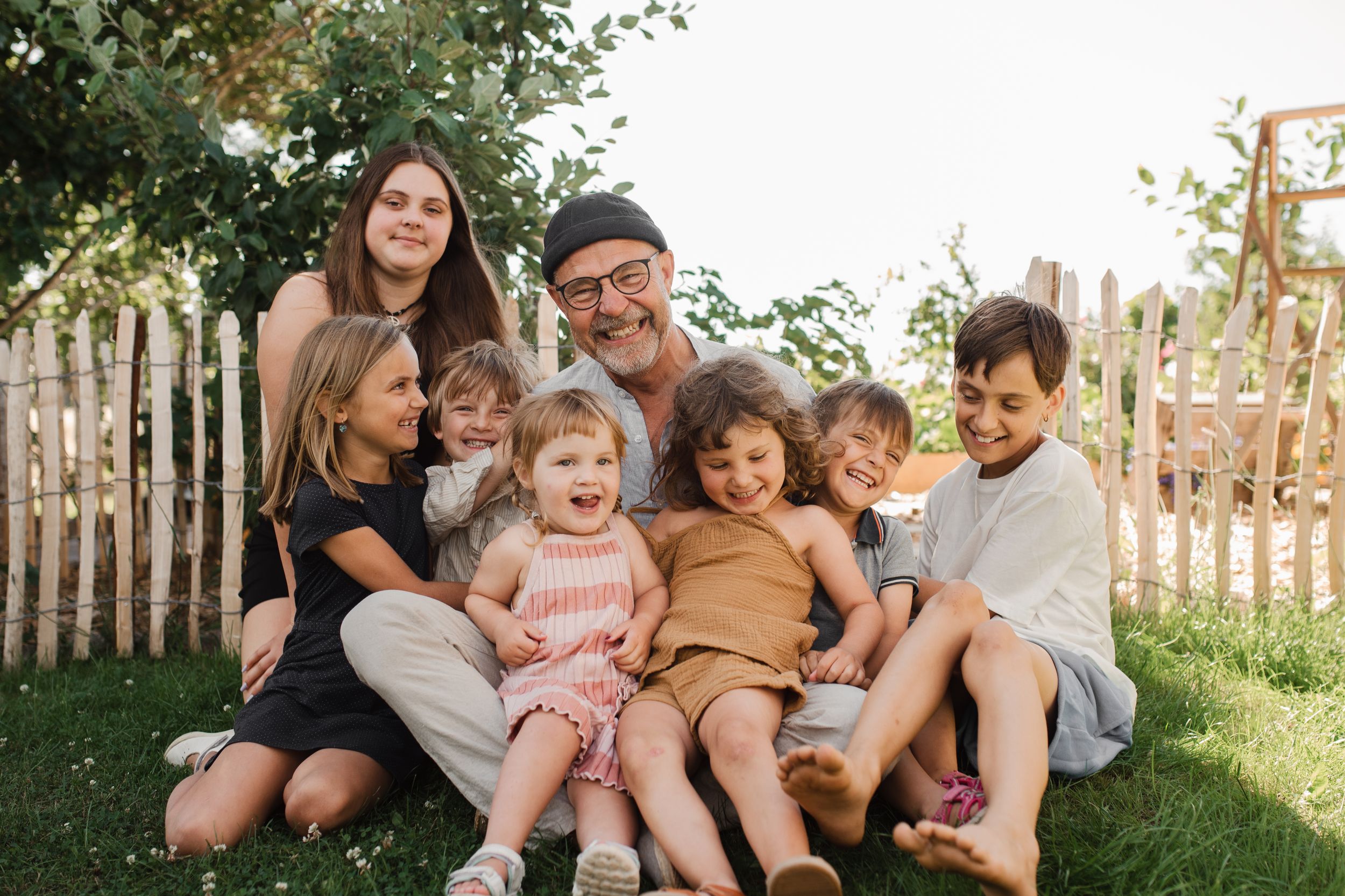 Extended family gathering outdoors on a sunny day with rustic fence in background.