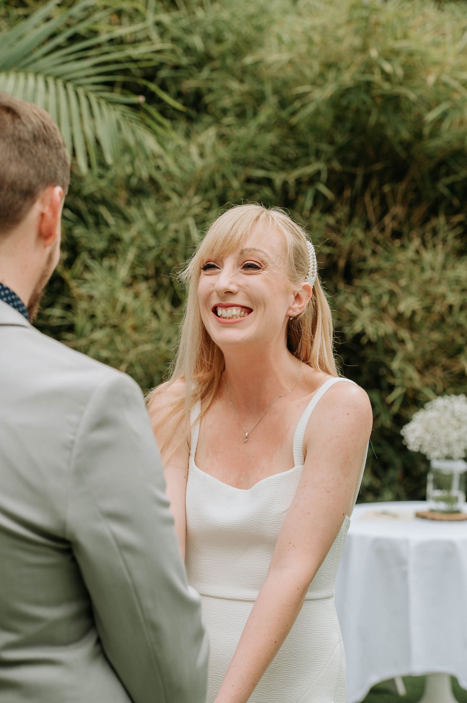 Happy moment during outdoor wedding ceremony with tropical foliage in background.