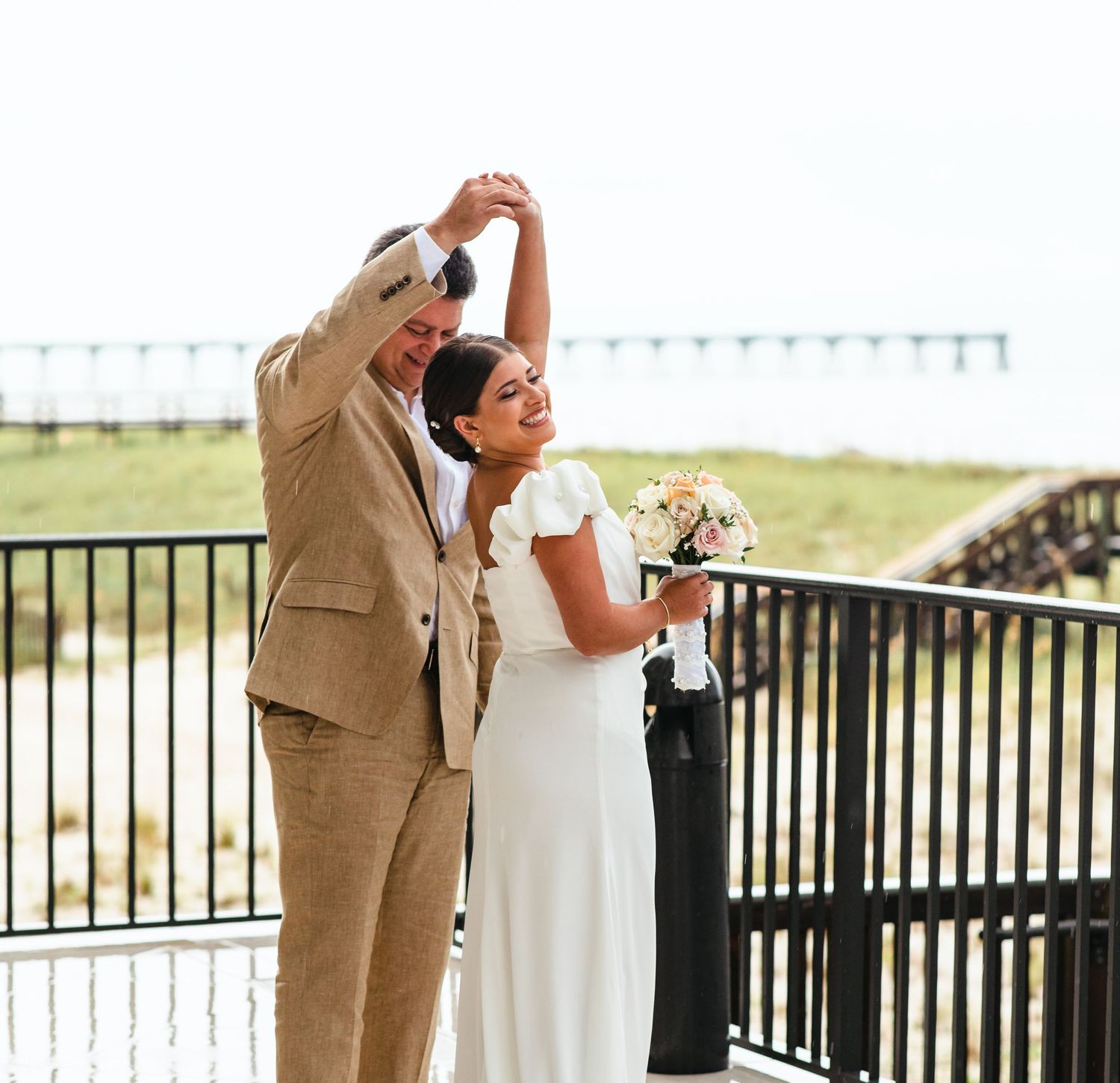 A couple dances playfully on a balcony overlooking the ocean.