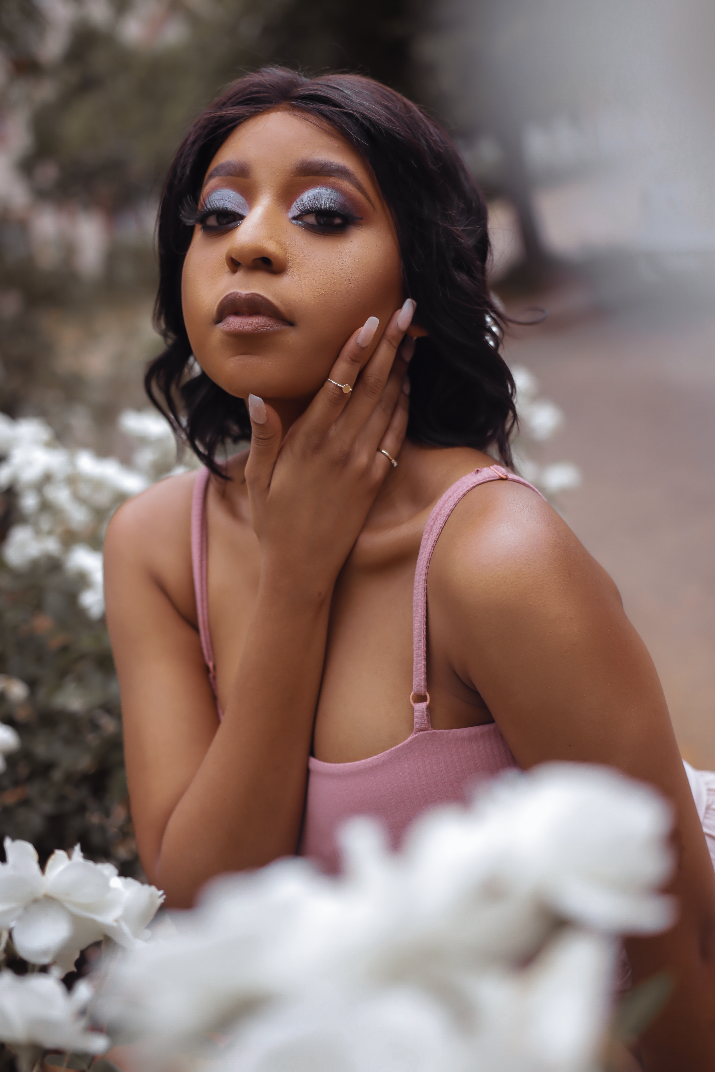 Artistic portrait in pink top with glamorous makeup amidst white flowers.