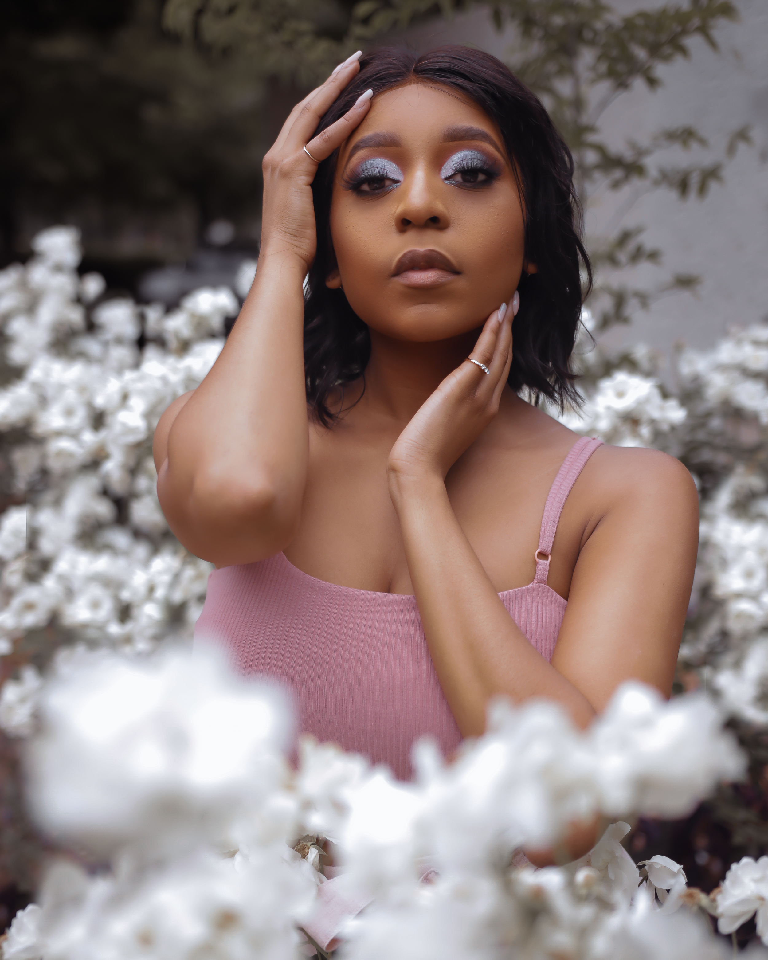 Dreamy portrait in pink top surrounded by white flowers with blue eyeshadow.