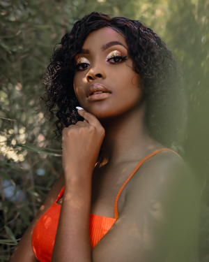 Portrait in orange top with curly hair against soft natural bokeh background.