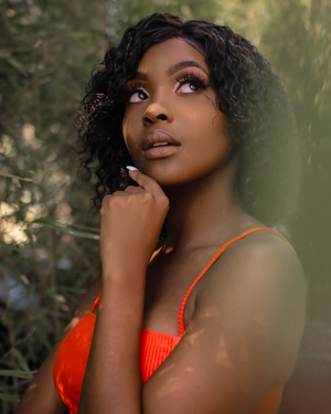 Upward gazing portrait in orange top with natural foliage backdrop.