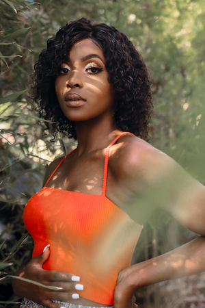 Fashion portrait of a model in orange tank top against blurred natural background with sunlight.