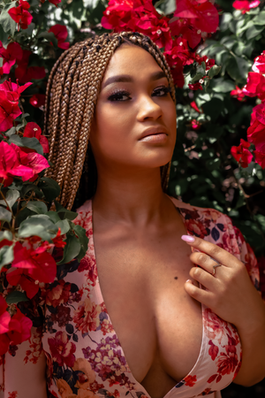 Glamour portrait amidst vibrant red roses wearing a floral printed dress.