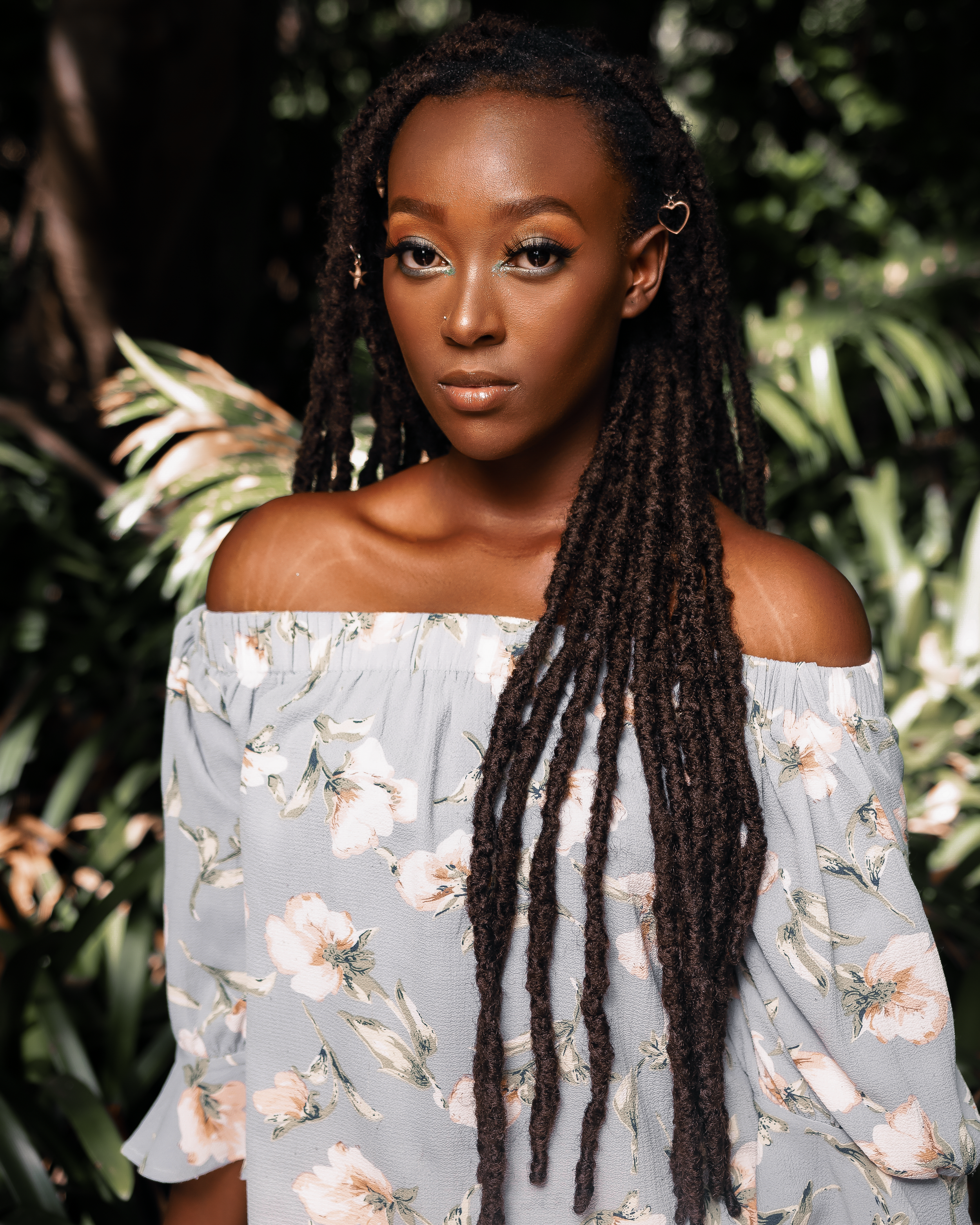 Portrait in floral off-shoulder dress with long braids against tropical foliage.