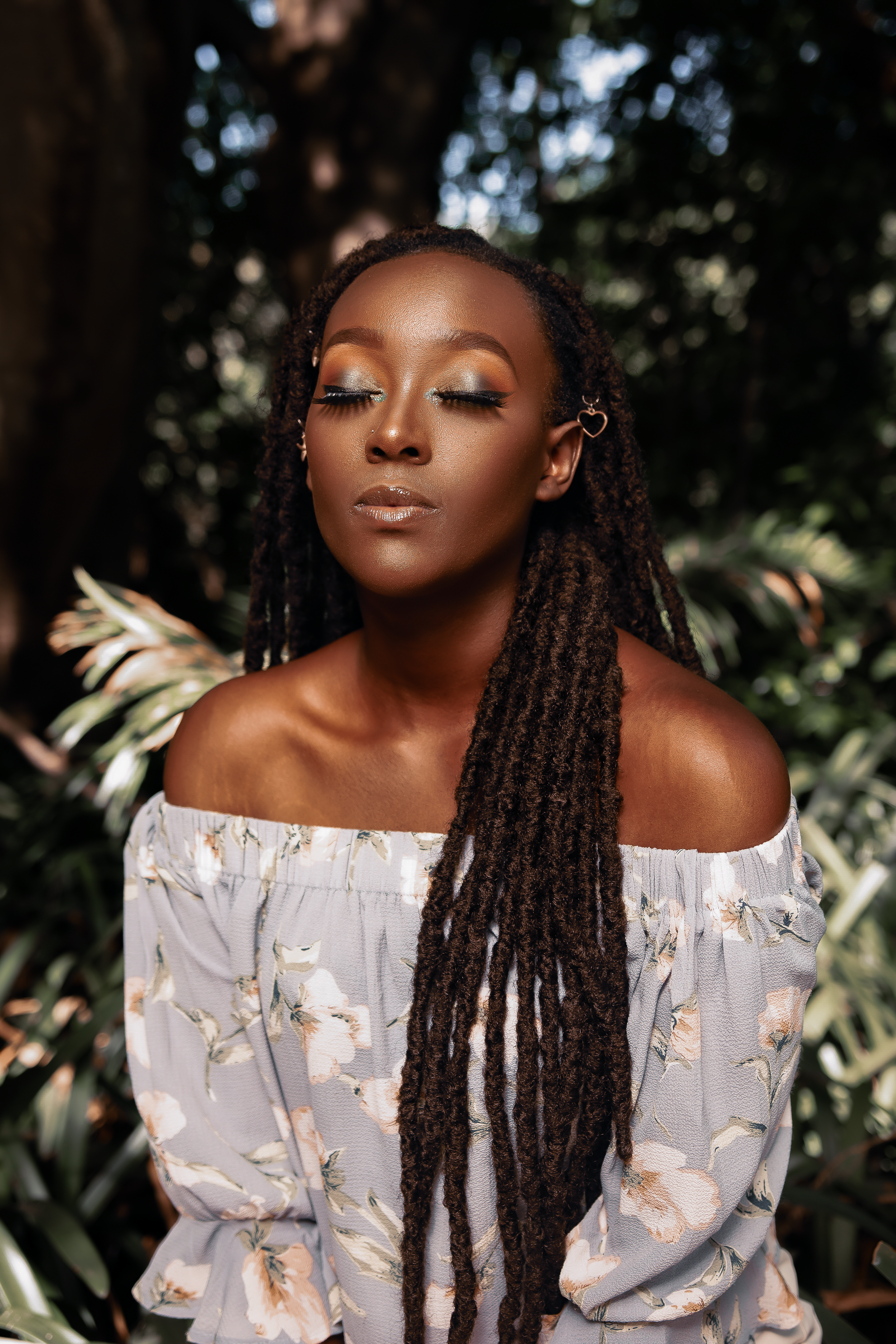 Close-up portrait in floral white dress with long braids against garden backdrop.