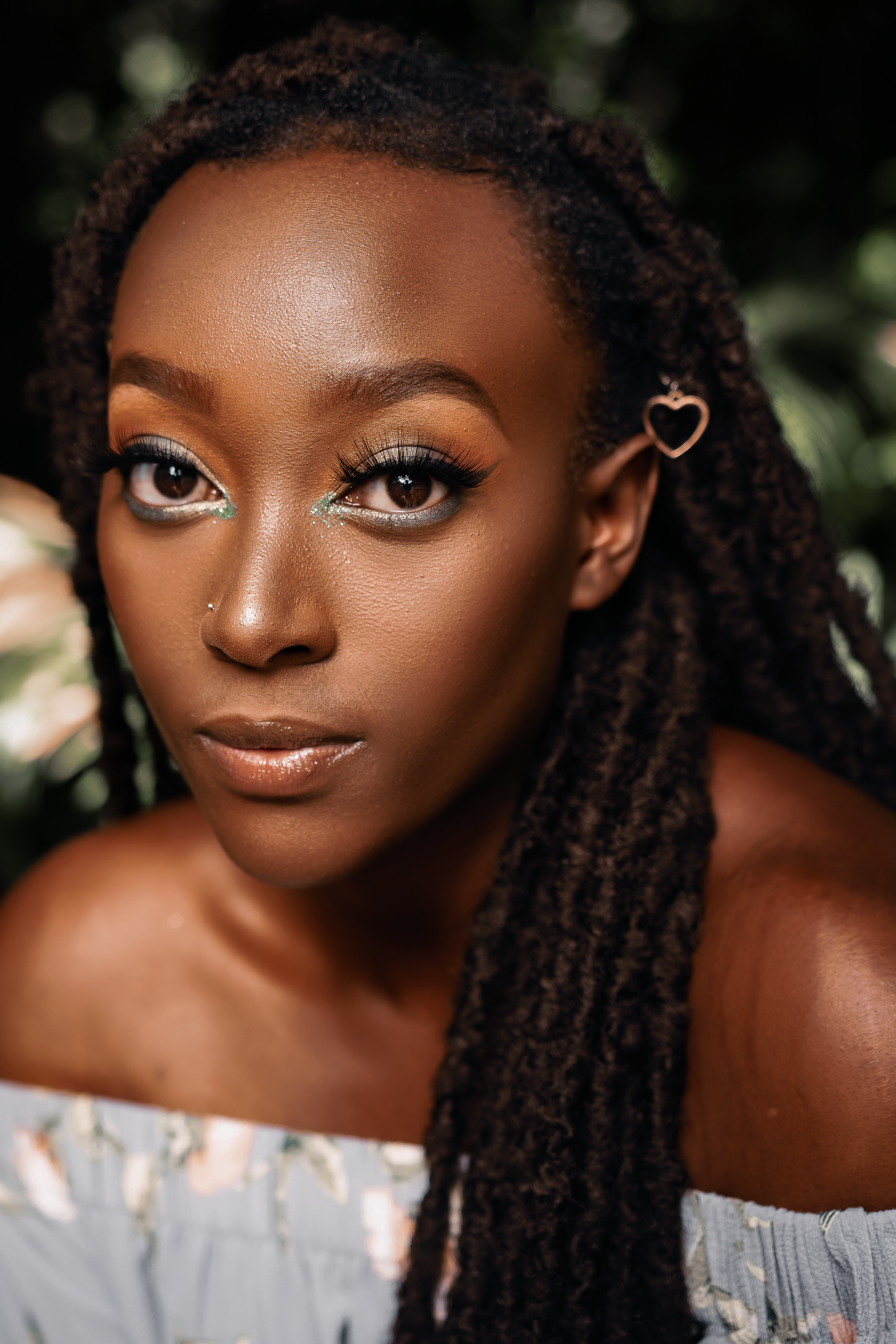 Close-up beauty shot with heart earring and braids wearing white off-shoulder top.