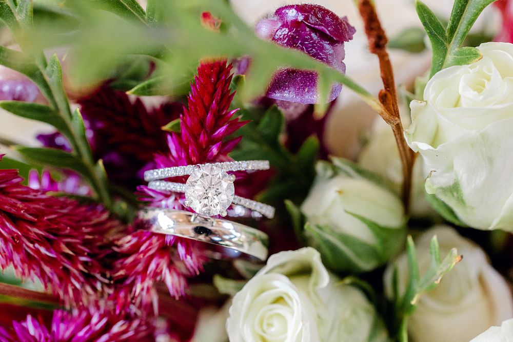 Diamond engagement ring and wedding bands nestled among white roses and purple flowers.