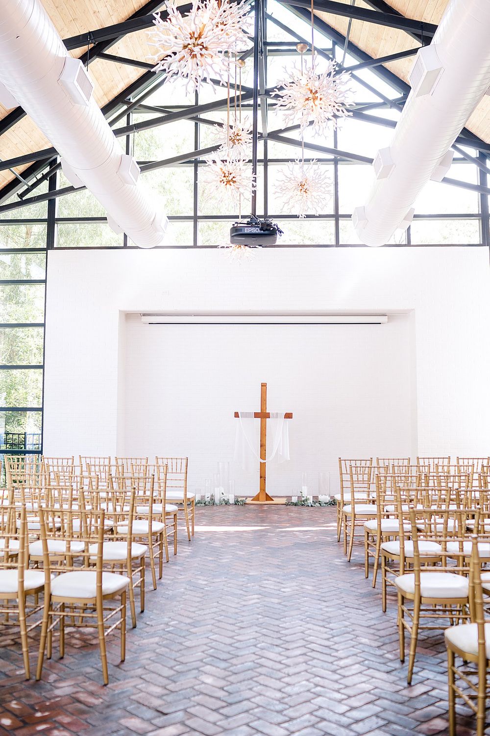 Modern church interior with herringbone brick floor, gold chairs and starburst chandeliers.