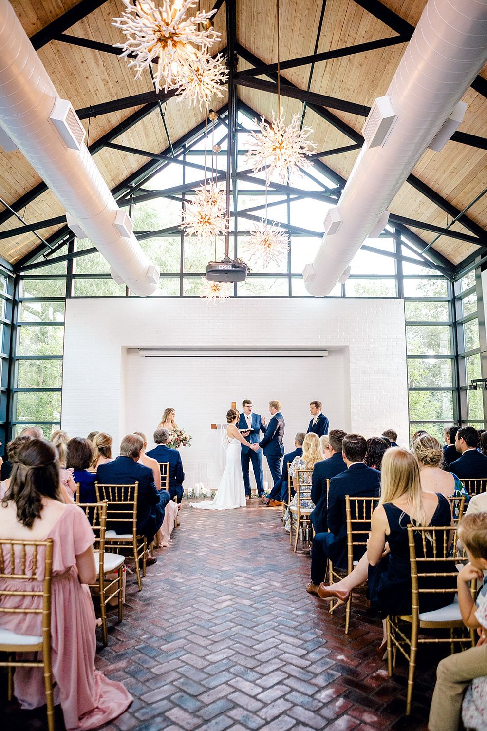 Wedding ceremony in progress under dramatic vaulted ceiling with starburst chandeliers.
