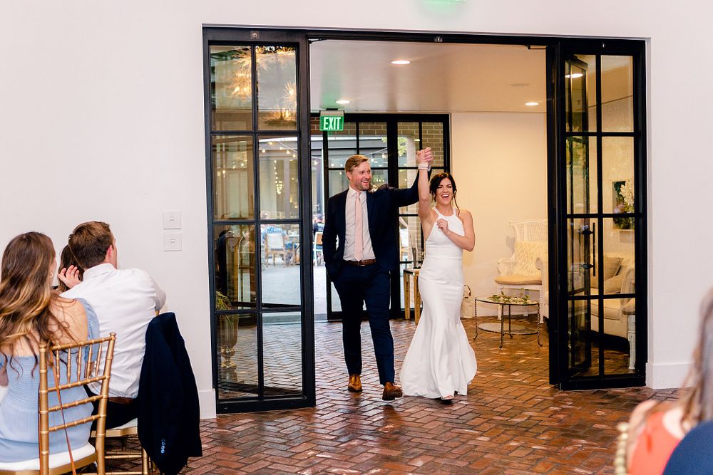 Wedding couple makes grand entrance through glass doors to reception venue amid applause.
