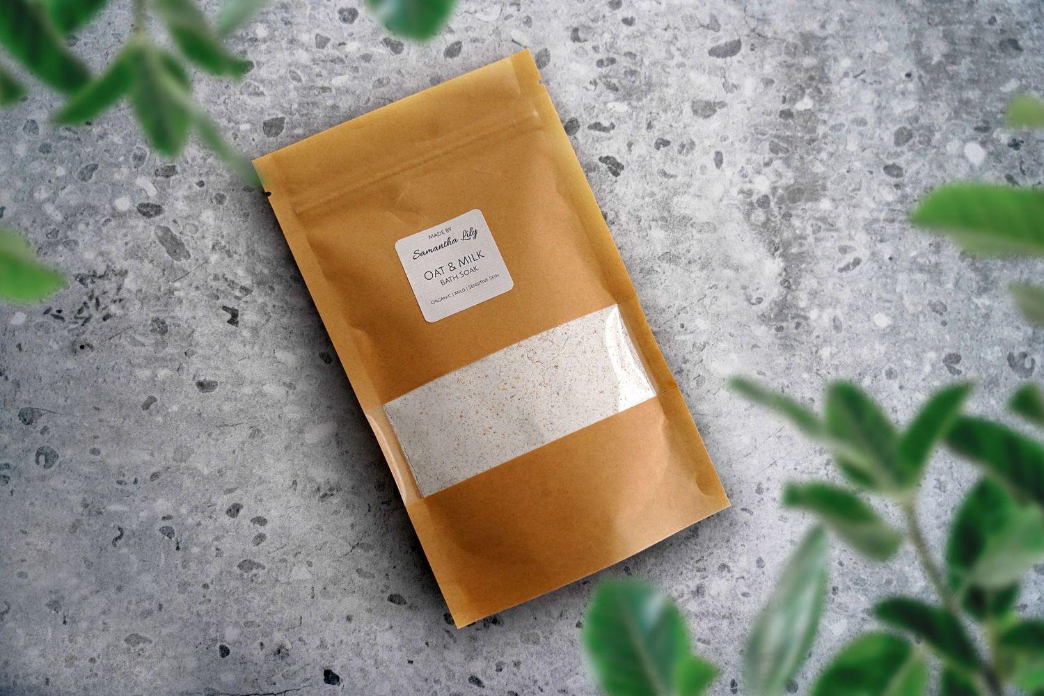 Brown kraft paper pouches arranged on concrete surface with green plant leaves in frame.