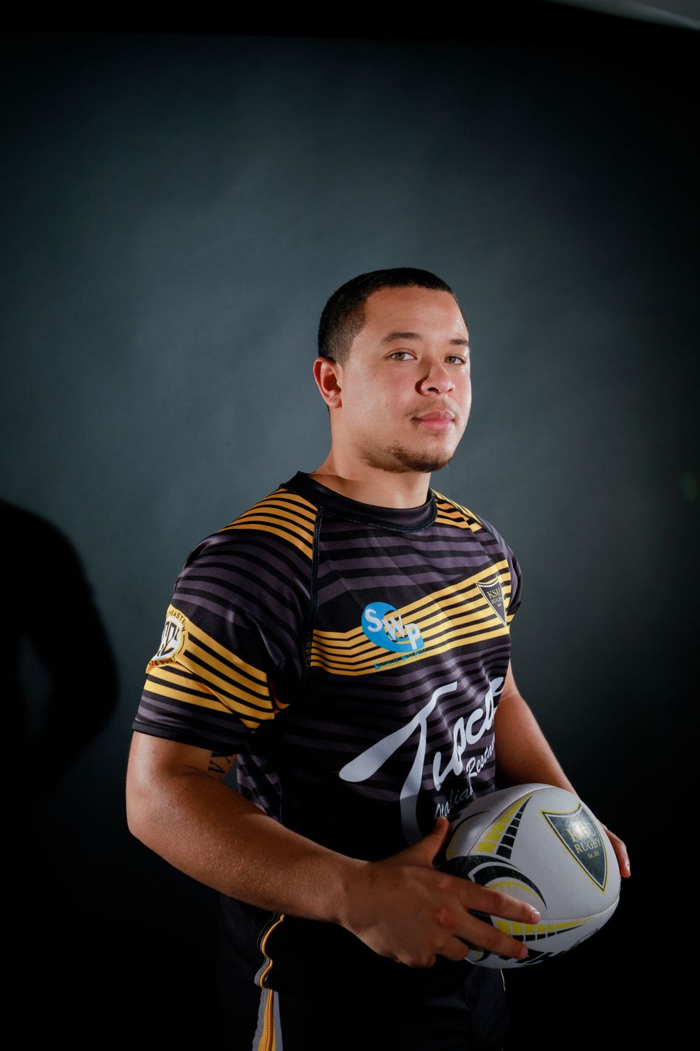 Rugby player in striped uniform holds ball while posing for professional sports portrait.