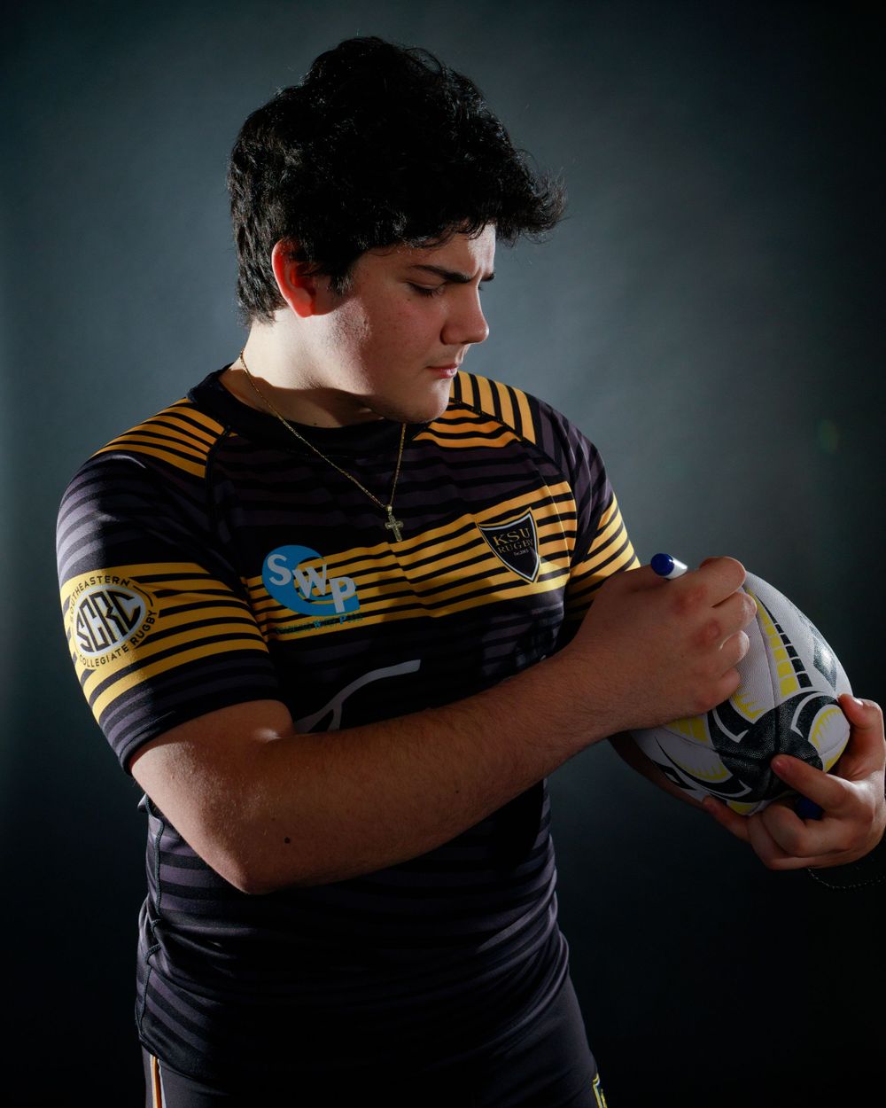 Rugby player examines ball while wearing black and gold striped uniform.