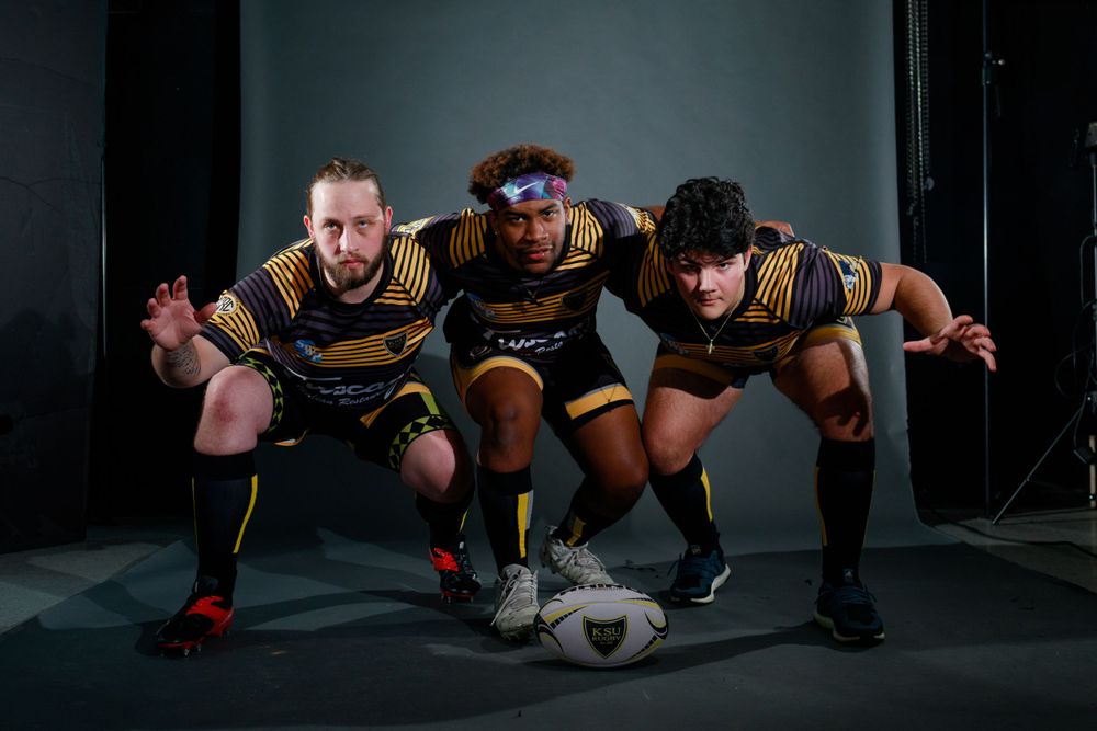 Rugby players demonstrate proper scrum formation technique on dark field.