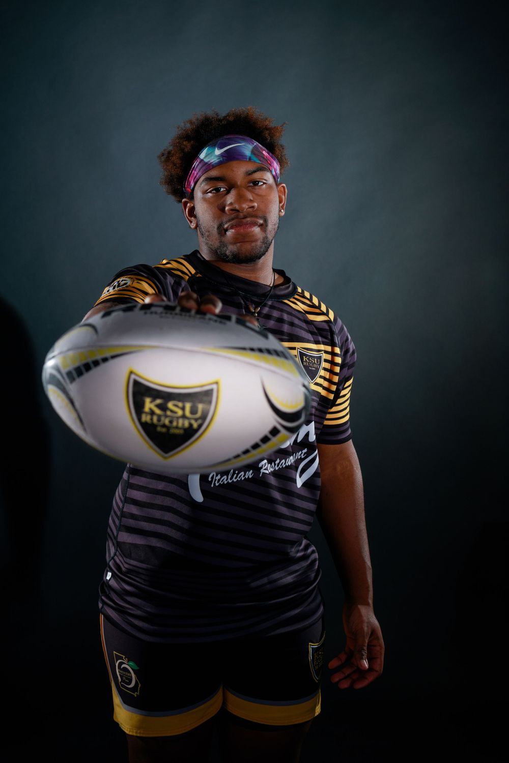Rugby team members in striped jerseys hold ball in dramatic studio lighting.