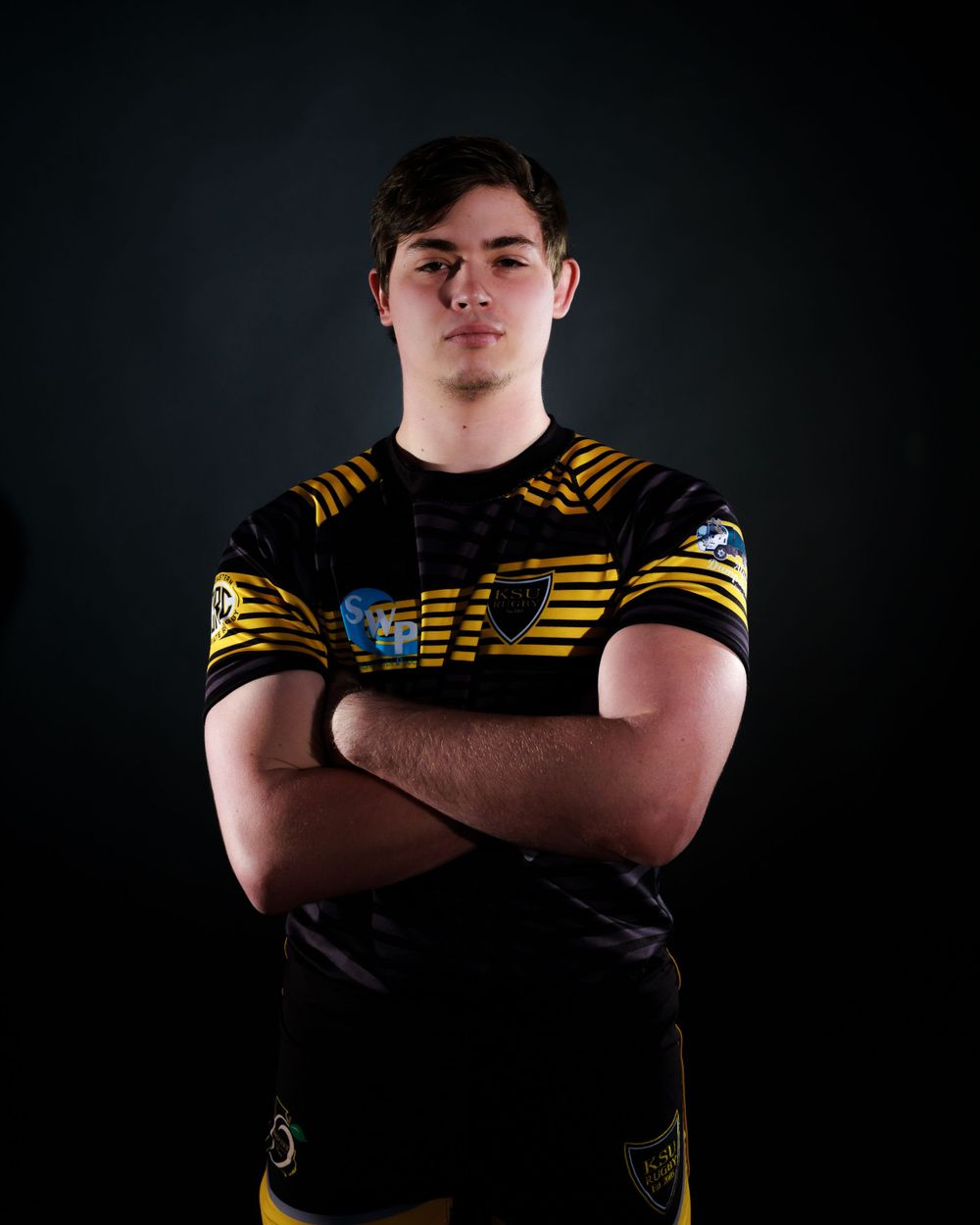 Athletic figure poses in black and yellow striped sports uniform against dark background.