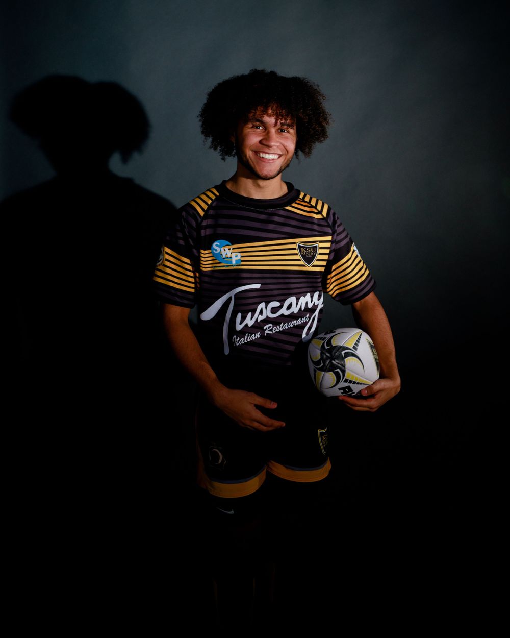 Rugby players in team uniforms hold ball in dramatic studio lighting sequence.