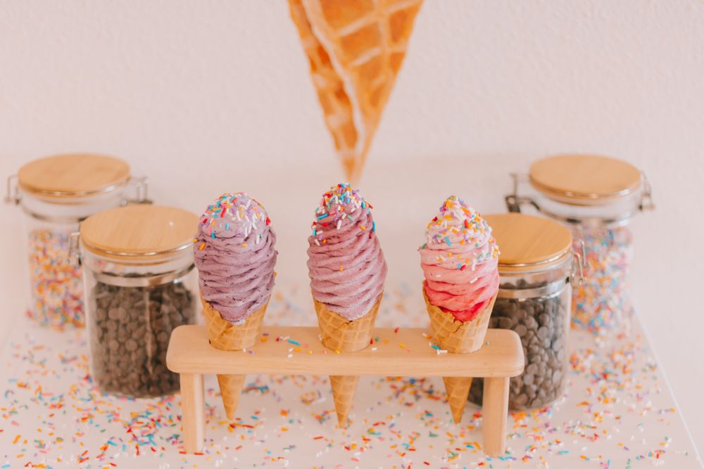 3 ice cream cones in a holder four jars of toppings behind sprinkles on table top