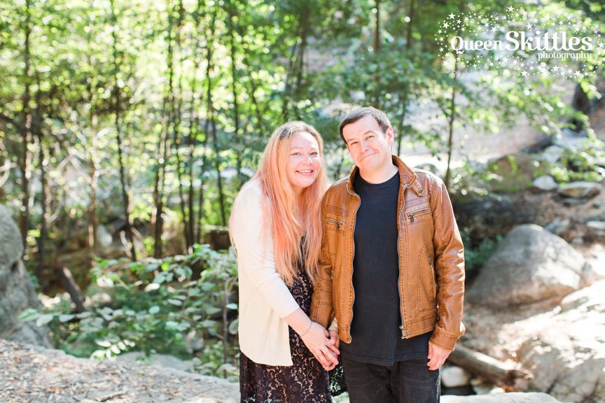 A couple poses together outdoors with autumn trees in the background.
