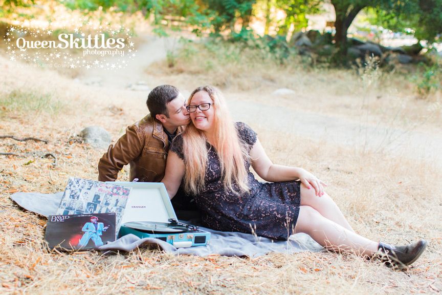 A couple relaxes on a picnic blanket in a sunny meadow setting.