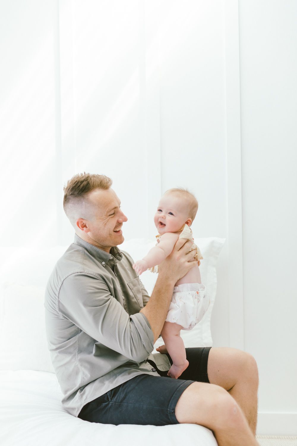 Parent plays with smiling baby during casual indoor photo session.