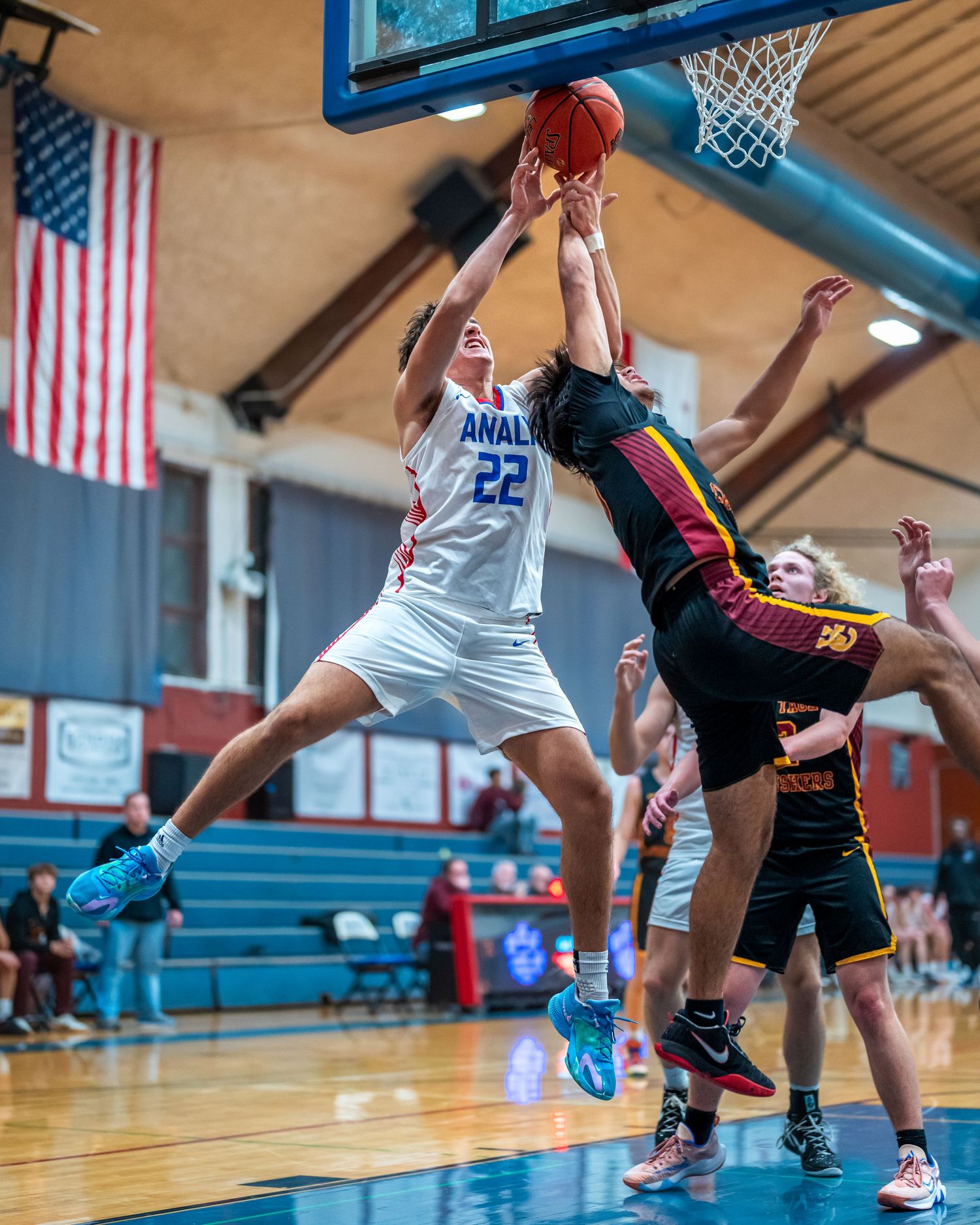 Basketball players leap for rebound under backboard during competitive indoor game.