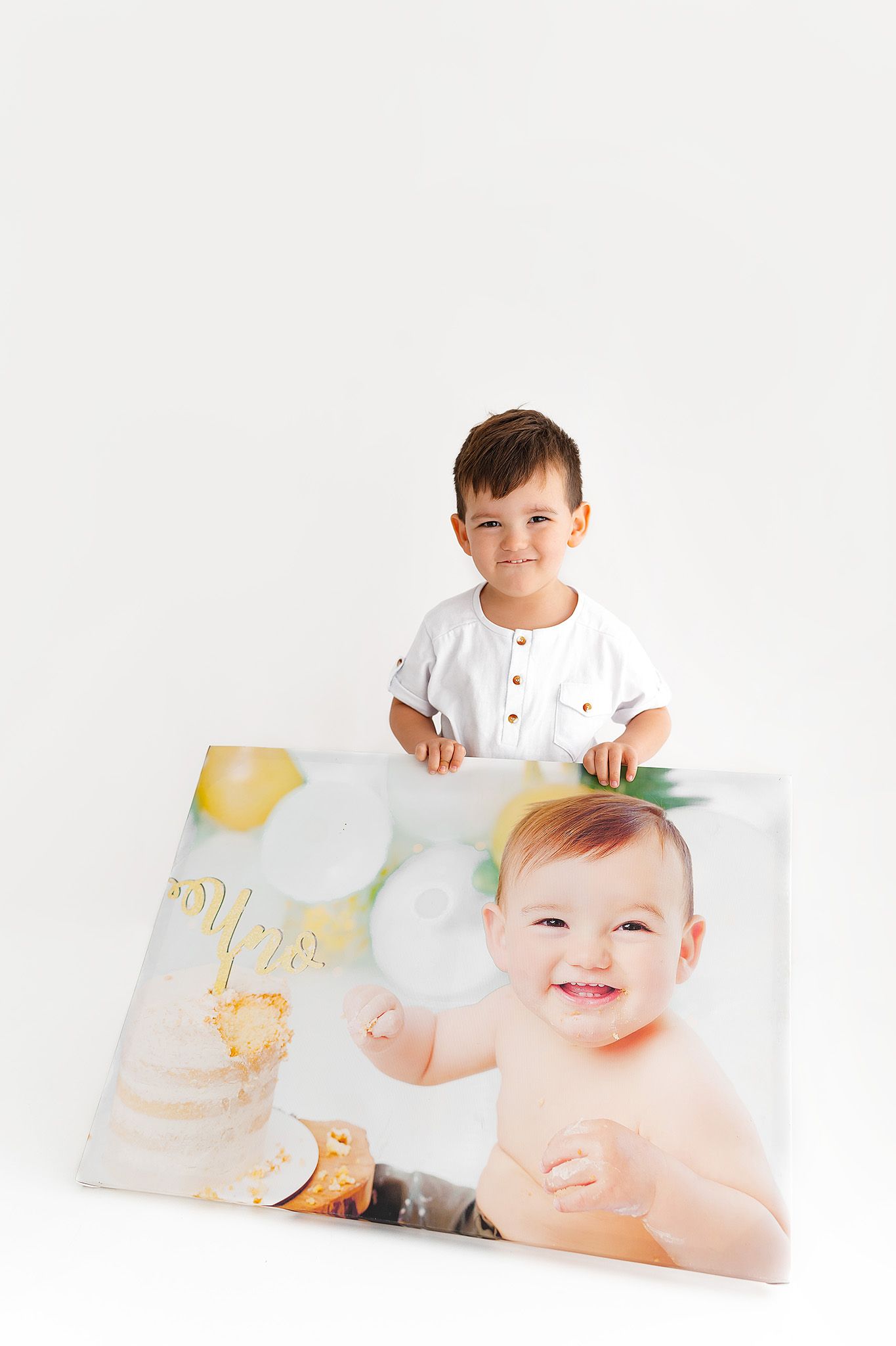 Child in white henley shirt displaying large printed photo canvas against white background.
