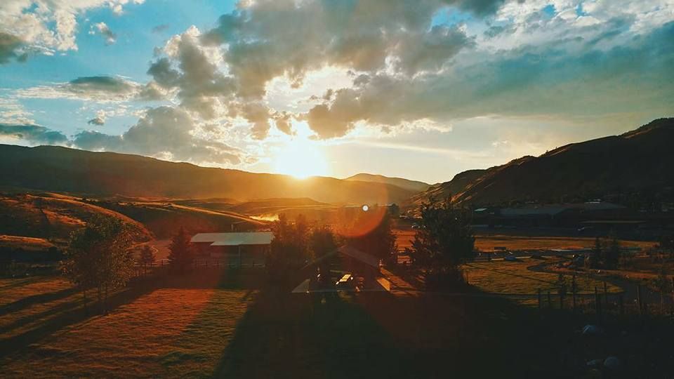 Golden sunset over rolling hills with silhouetted buildings and dramatic clouds.