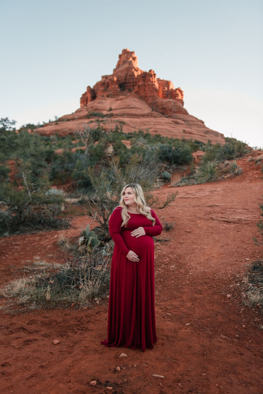 A person in a flowing red velvet dress poses against the backdrop of red rock formations in Sedona.