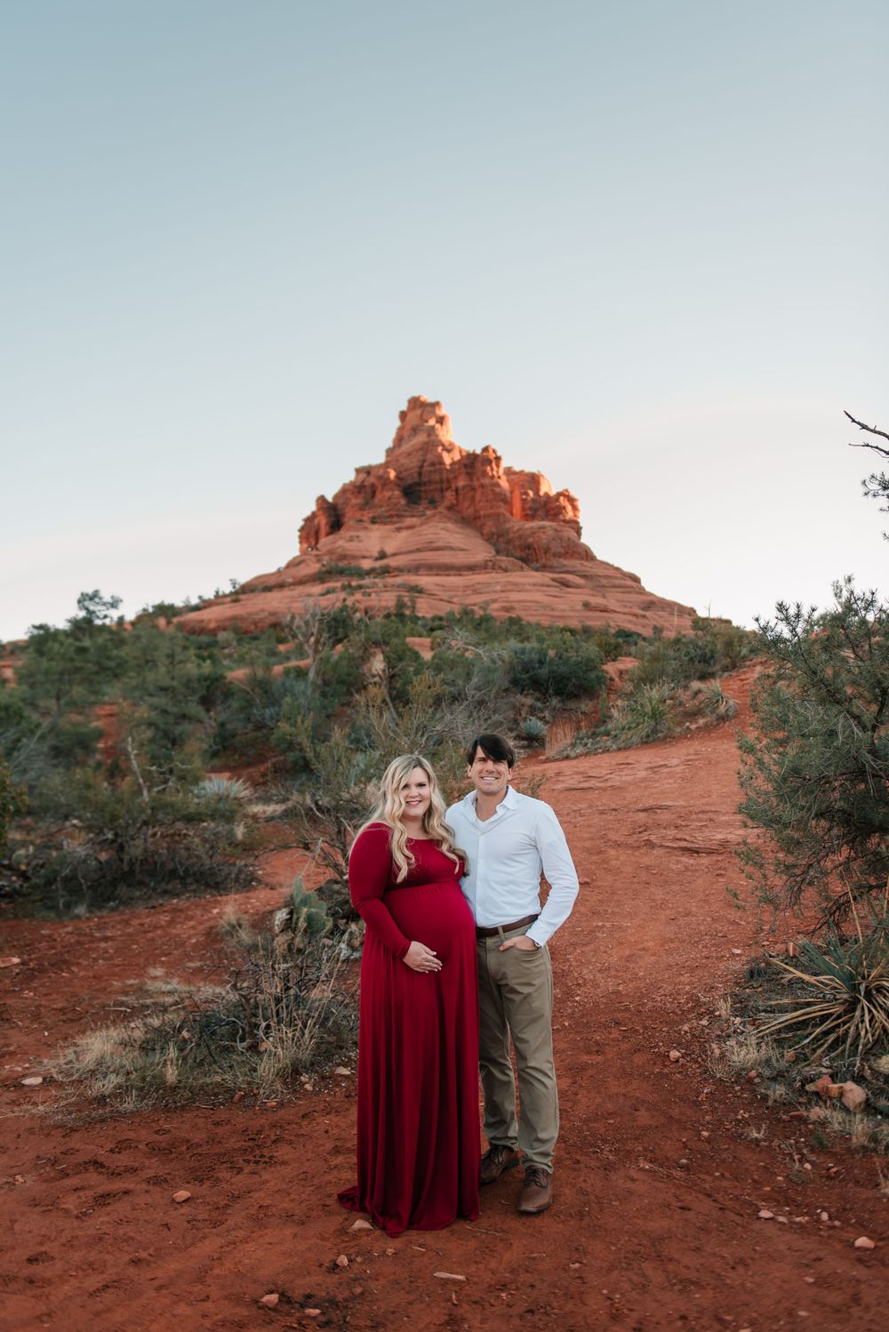 A couple poses together on red rocks with Bell Rock formation visible in the background.