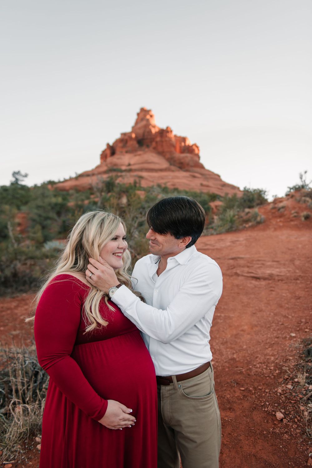 A tender embrace between expectant parents with Bell Rock formation in the desert background.