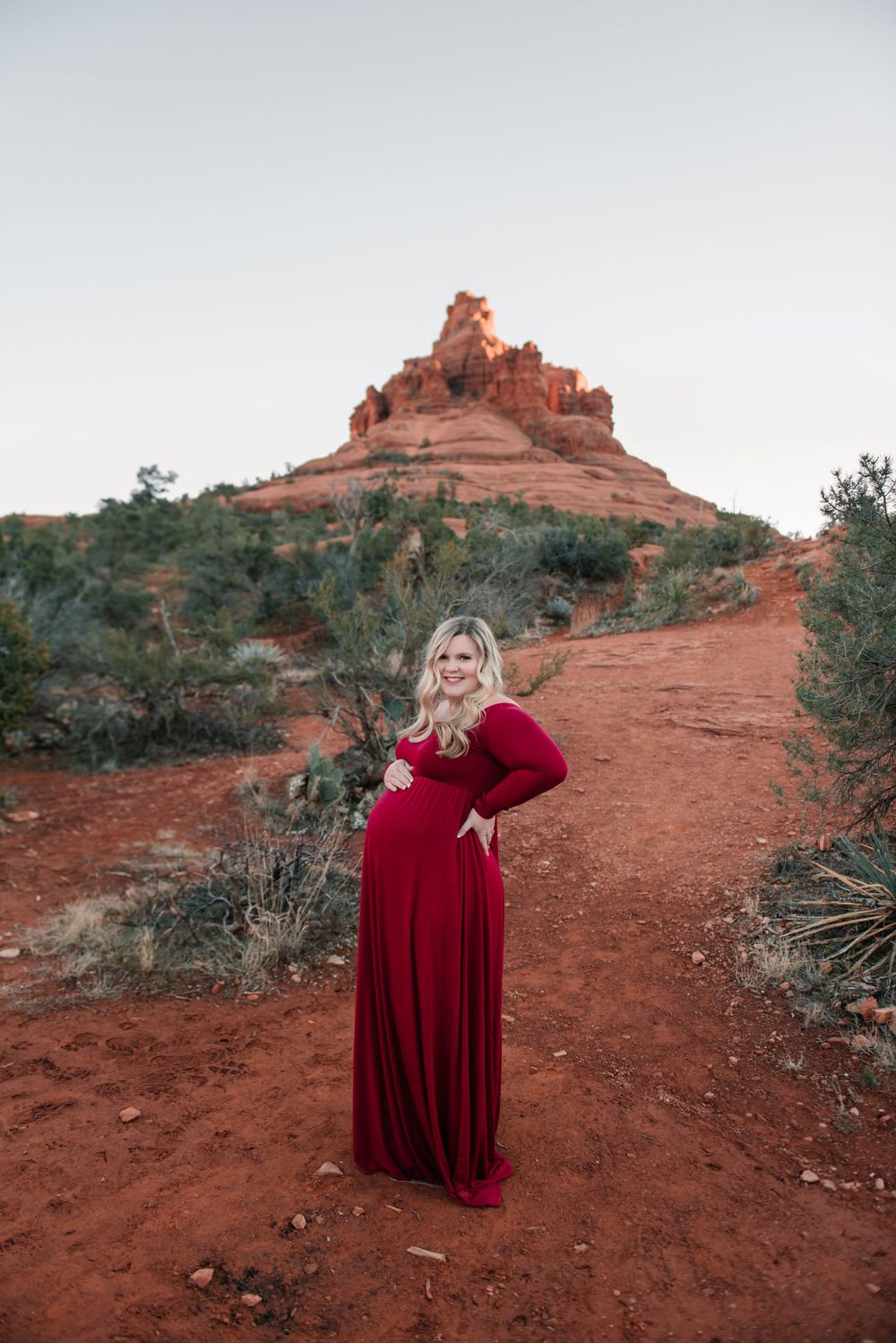 A maternity portrait featuring a burgundy dress against the dramatic red rocks of Sedona.