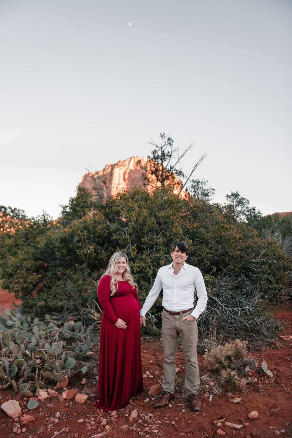 A couple shares a moment during their maternity photoshoot with desert scenery in the background.