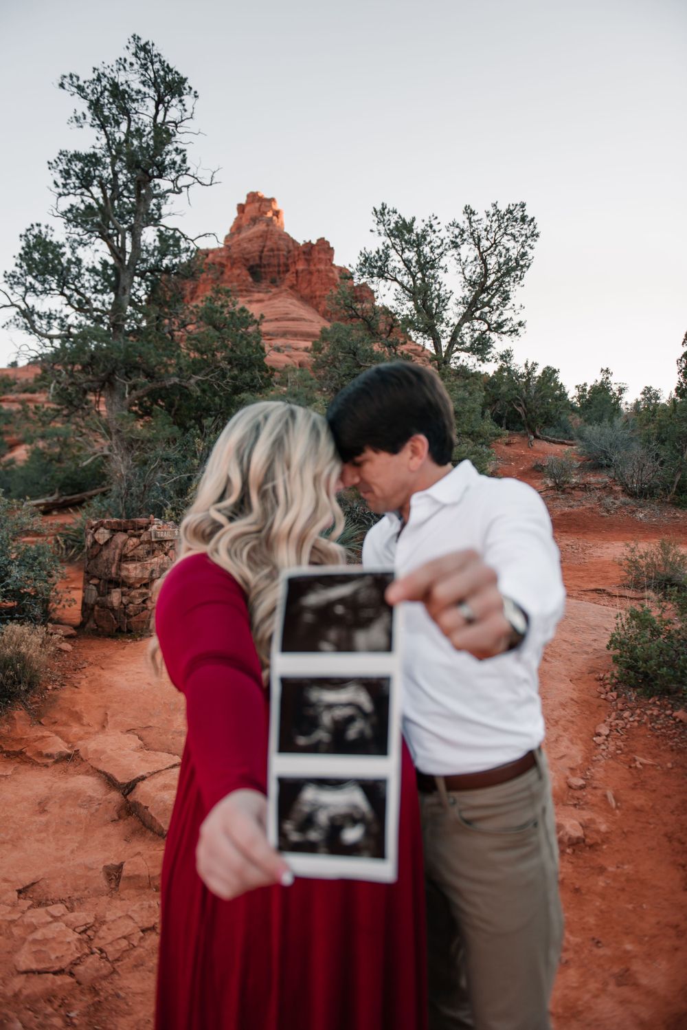 A couple shows their ultrasound photo during a pregnancy announcement photoshoot in a desert setting.