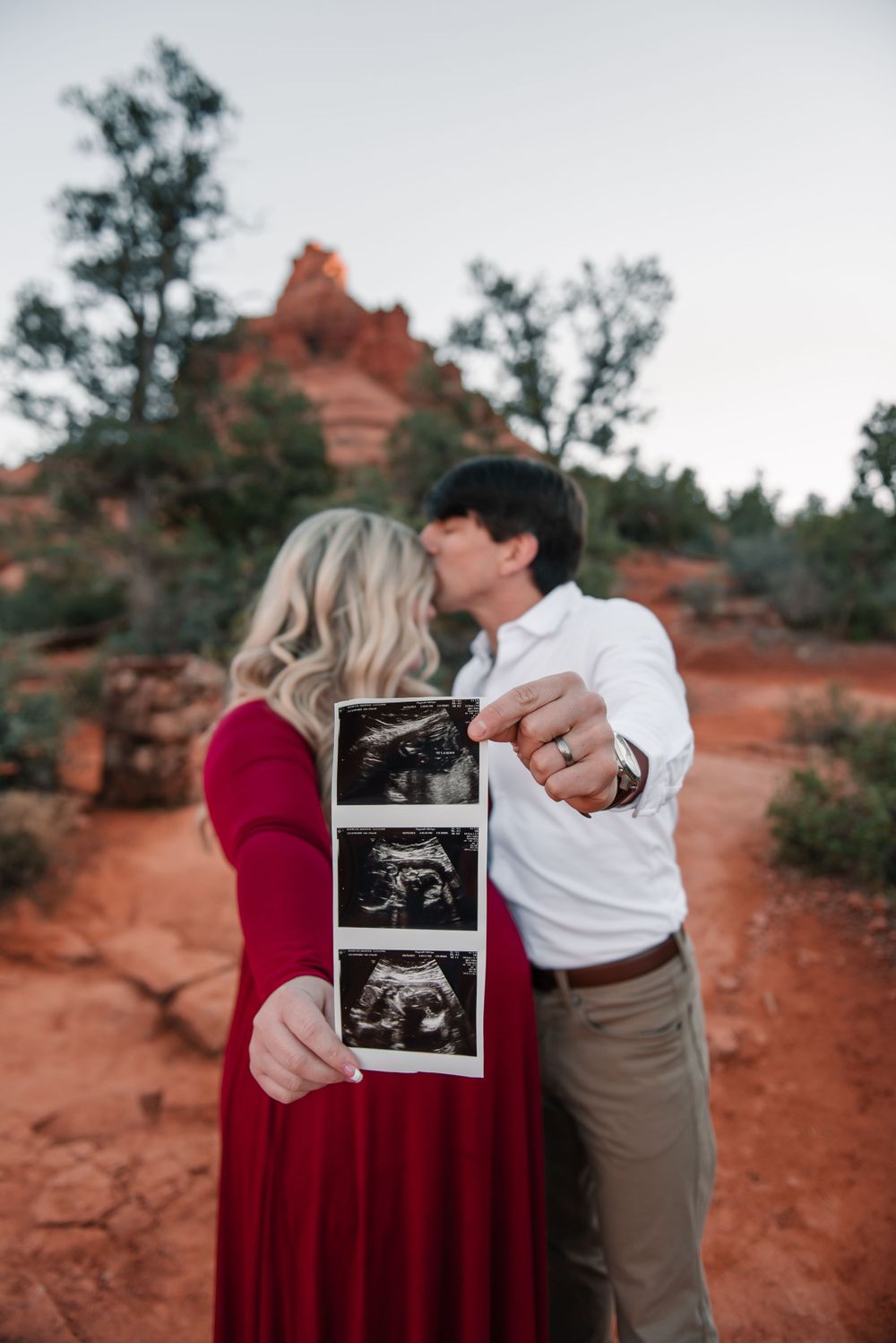 A couple shares their ultrasound photo while standing on red rock terrain during sunset.