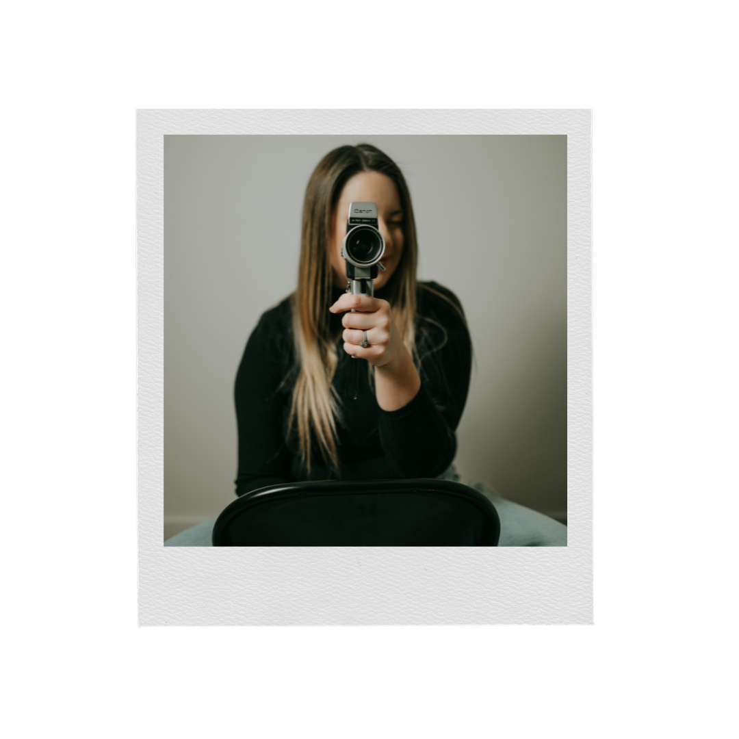 Creative self-portrait photograph with vintage camera against neutral background.