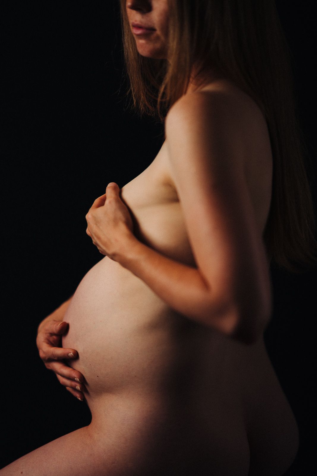Artistic silhouette of a pregnant woman's belly against dark background.