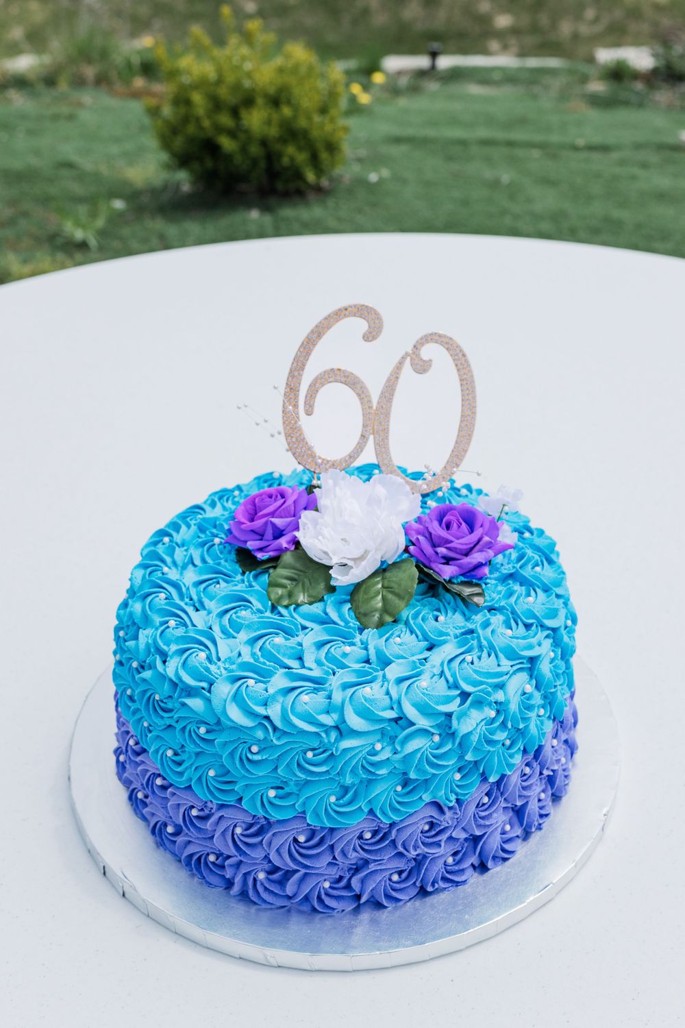 Blue and purple ombre birthday cake decorated with roses and a gold number 60 topper.