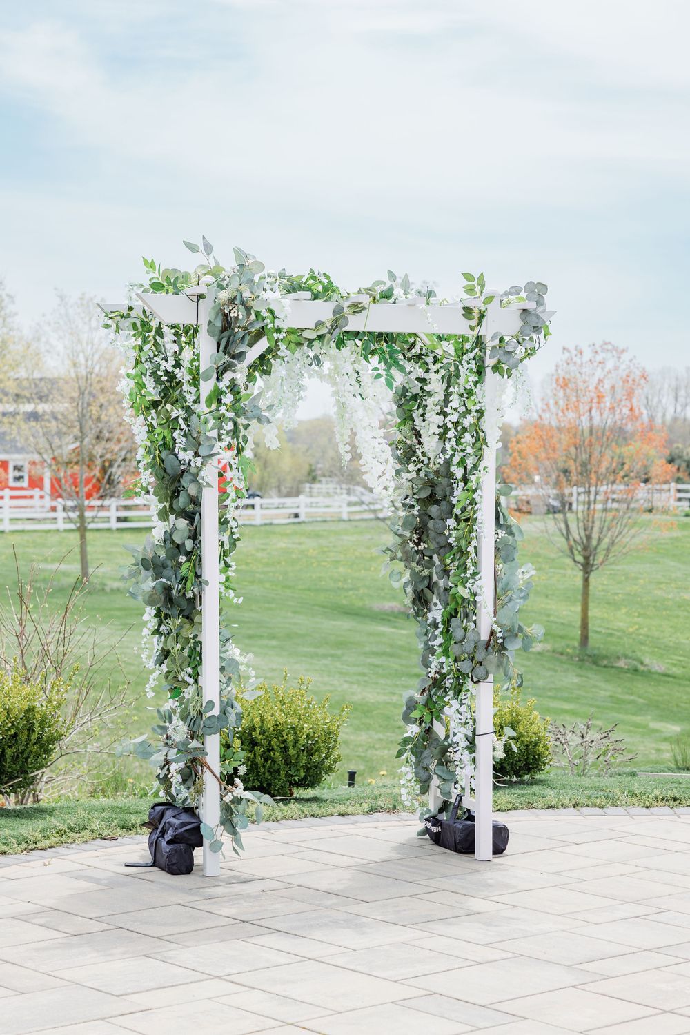 White wedding arch decorated with greenery and flowers in outdoor garden setting.