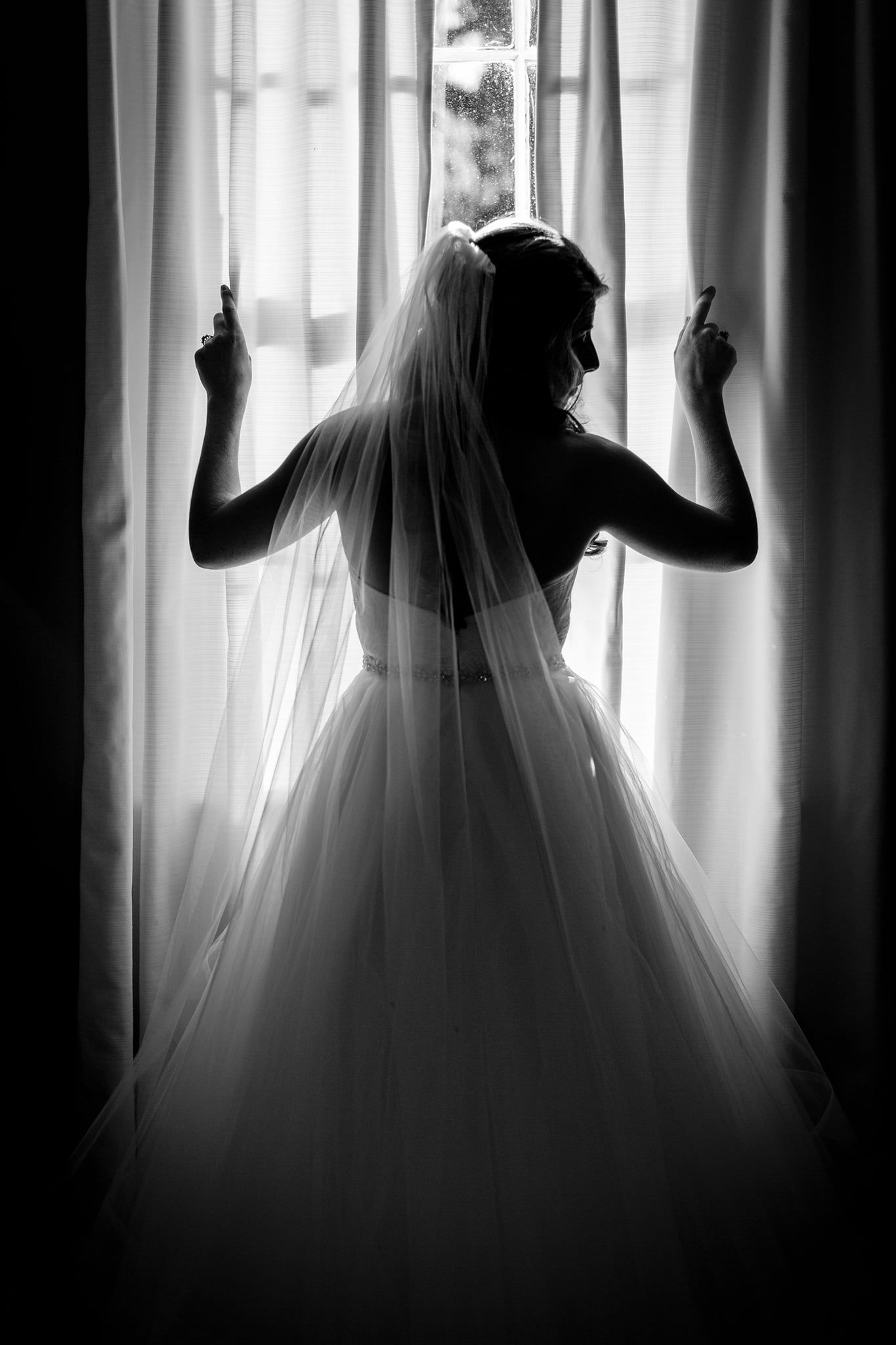 Black and white bride peeks over shoulder in front of window