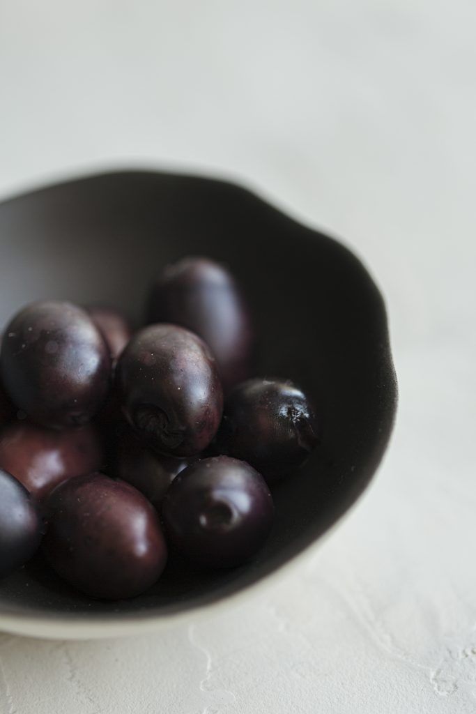 Fresh dark purple grapes in a black ceramic bowl on white surface.