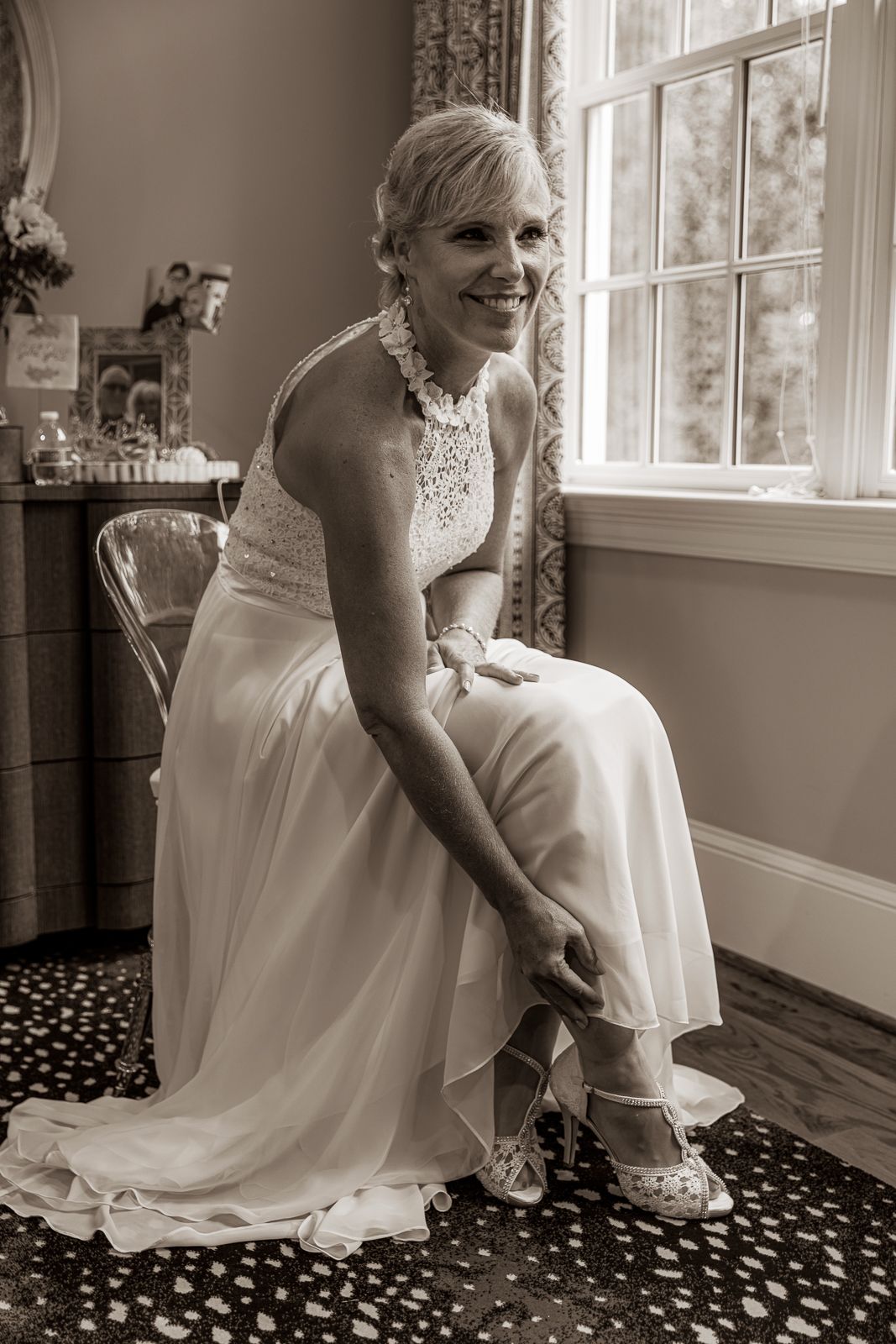 Bride in white dress sitting by window in black and white sequence showing joyful preparation moments.