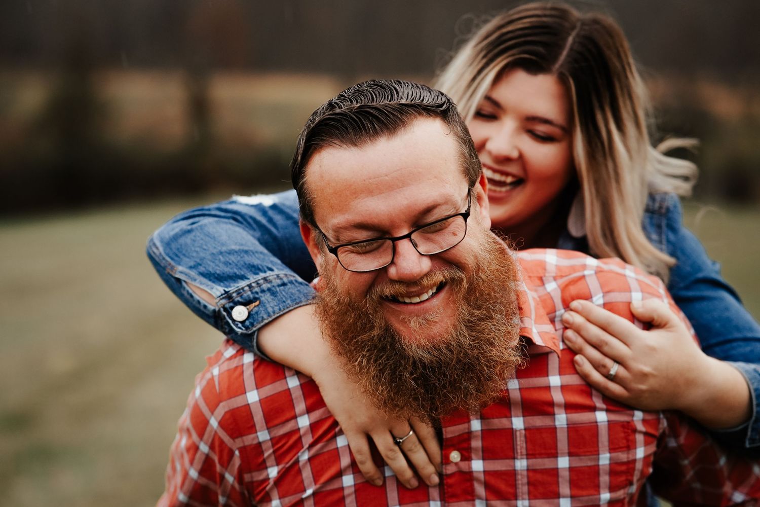 Playful couple laughing during outdoor photoshoot with man in red plaid shirt.