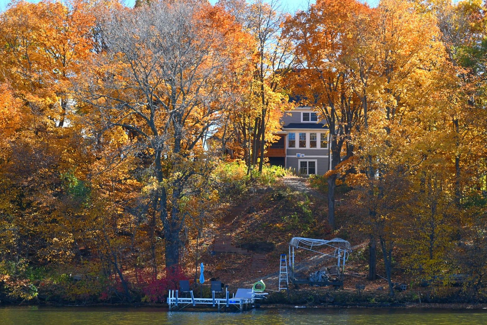 Autumn trees frame a lakeside house with a dock during peak fall foliage.
